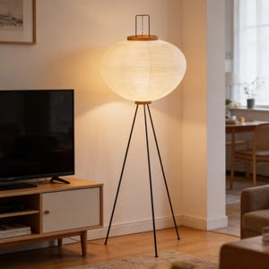 May include: A modern floor lamp with a large, round, paper lantern shade. The shade is cream-colored and rests on a wooden base and black metal tripod legs. The lamp is a stylish addition to any living space.