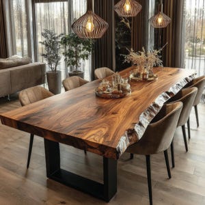 May include: A large, solid wood dining table with a live edge and a dark brown finish. The table is supported by a black metal base and surrounded by upholstered chairs. Decorative items are placed on the table, and pendant lights hang above.