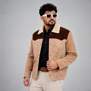 May include: A tan and dark brown suede jacket featuring a cream-colored faux shearling collar, a button-front closure, and two front pockets. The jacket is worn over a black button-down shirt and paired with light-colored trousers and a brown belt.