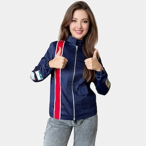 Könnte beinhalten: Marineblaue Reißverschlussjacke mit rotem Streifen auf der Vorderseite und Aufnähern auf den Ärmeln. Die Jacke hat einen hohen Kragen und zwei Vordertaschen. Das Model trägt eine graue Jeans.