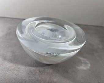 May include: A clear glass bowl with a swirling white pattern. The bowl has a rounded shape with a circular opening at the top. The brand name "KOSTA BODA" is printed on the side.