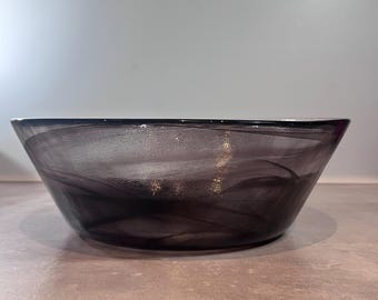 May include: A decorative glass bowl with a dark purple, swirling pattern. The bowl has a wide, shallow shape and a smooth, glossy finish. The bowl is suitable for serving or display.