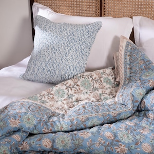 Può includere: Un letto con una trapunta a fantasia floreale azzurra e un cuscino abbinato. La trapunta ha un motivo floreale bianco al centro e un bordo azzurro. Il cuscino ha un motivo blu ripetuto. Il letto è fatto con lenzuola bianche.