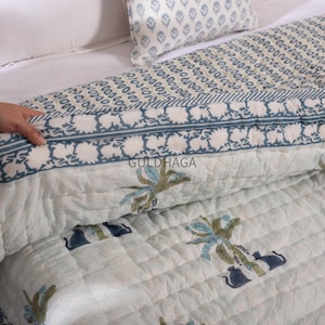 May include: A quilted bedspread and pillow set with a floral and geometric pattern in shades of white and blue. The bedspread features a repeating floral design and a contrasting border. The pillow has a similar pattern. The brand name "GULDHAGA" is visible.
