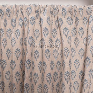 May include: Beige curtain with a repeating blue floral pattern. The fabric is gathered at the top, creating soft folds. The text "GULDHAGA" is printed on the fabric.