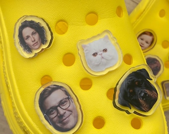 May include: A bright yellow clog shoe featuring several clear acrylic charms attached to the ventilation holes. The charms display various photographic portraits, including a woman, a man with glasses, a white cat, and a black dog.