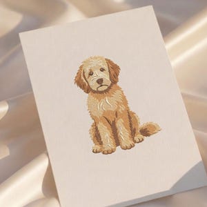 Puede incluir: Una tarjeta rectangular de color blanco roto con una ilustraci&oacute;n detallada bordada a m&aacute;quina de un cachorro de color dorado sentado. El cachorro tiene pelaje texturizado, orejas ca&iacute;das y nariz oscura en tonos beige, oro y marr&oacute;n.