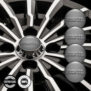 May include: Close-up of a black and silver car wheel with a central hubcap. The hubcap and wheel spokes have the text "YOUR WHEEL BRAND HERE". Additional hubcaps with the same text are visible. The wheel has a "CUSTOM MADE" and "100% PREMIUM QUALITY" sticker.