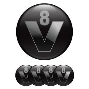 May include: A glossy black emblem featuring a silver "V" shape with the number "8" above it. Four smaller versions of the emblem are below the larger one. The design has a metallic, reflective appearance.