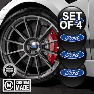 May include: A set of four black Ford wheel centre caps with a blue Ford logo. The image also shows a car wheel with a silver rim, a red brake caliper, and the text "CUSTOM MADE".