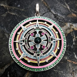 May include: A silver pendant with a colorful, intricate design. The pendant features a central dark green stone surrounded by pink, green, and purple gems. The outer ring has a pink, blue, yellow, and green enamel design. The pendant has a silver bail.