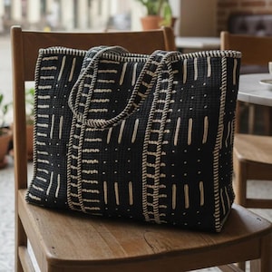 May include: A rectangular tote bag featuring a black fabric base with a repeating pattern of cream-colored vertical lines, dashes, and dots. The bag has two matching fabric handles and a structured shape with visible stitching along the edges.