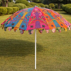 May include: A vibrant, colorful outdoor umbrella with a white pole. The umbrella's canopy features intricate patterns in shades of pink, blue, orange, and yellow. The edges are adorned with decorative tassels.