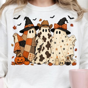 Könnte beinhalten: Ein weißes Sweatshirt mit einer Grafik von drei Geistern. Der linke Geist trägt einen Hexenhut und hat ein Patchwork-Muster. Der mittlere Geist trägt einen Cowboyhut und ein Kuhfellmuster. Der rechte Geist trägt einen Hexenhut mit Schleife und Sternen.