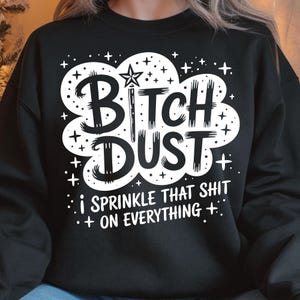 May include: Black sweatshirt with the text "Bitch Dust" in a white cloud design, with a star-topped wand and the phrase "I sprinkle that shit on everything." The design includes small star accents.