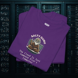 May include: Two purple t-shirts are stacked, featuring a graphic of a guru with the text "Salty Guru" and "The Cloud Is Just Someone Else's Computer." The guru is depicted with a long white beard and glasses, seated in a meditative pose.
