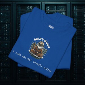 Może przedstawiać: Dwie królewskie niebieskie koszulki z grafiką guru z napisem "Salty Guru" i "$ sudo apt-get install coffee". Guru ma długą białą brodę i okulary, siedząc w pozycji medytacyjnej.