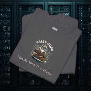 Może przedstawiać: Dwie ciemnoszare koszulki z napisem "Salty Guru" i ilustracją guru. Guru siedzi, nosi okulary i pokazuje znak pokoju. Na koszulkach wydrukowano również napis "Ping Me When It's Friday".