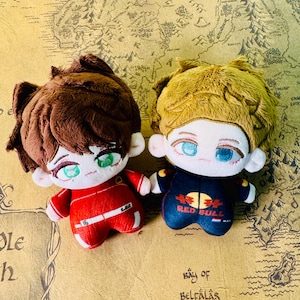 Peut inclure: Deux poup&eacute;es en peluche avec des traits de visage d&eacute;taill&eacute;s et des cheveux touffus. L'une porte une combinaison de course rouge avec le num&eacute;ro 16, l'autre une combinaison bleu marine avec un logo Red Bull. Les deux poup&eacute;es ont de grands yeux.