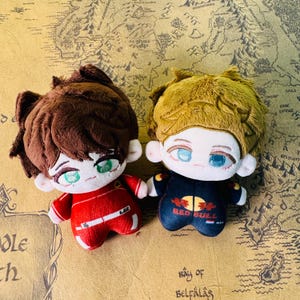 Peut inclure: Deux poup&eacute;es en peluche avec des traits de visage brod&eacute;s et des cheveux touffus. L'une porte une combinaison de course rouge avec le num&eacute;ro 16, l'autre une combinaison de course bleu marine avec le logo Red Bull. Les poup&eacute;es sont sur une carte.