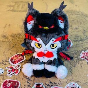 May include: A plush owl-like creature with a black top hat, red accents, and a red bow tie. The owl has yellow eyes and is primarily gray, black, and white. Stickers with illustrations are scattered around the plush toy.