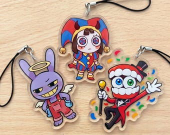May include: Three clear acrylic charms with black phone straps. One features a purple rabbit with a halo and wings in red overalls. Another shows a jester with a red and blue hat. The third depicts a red-toothed character in a tuxedo with confetti.