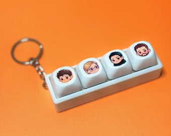 May include: A white keychain featuring four keyboard keycaps with cartoon faces. The keycaps are arranged in a row and attached to a silver chain. The background is a solid orange.