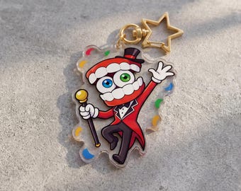 May include: A clear acrylic keychain featuring a cartoon character with a red coat, black pants, and a top hat. The character has a toothy grin, blue and green eyes, and is holding a cane. A gold star-shaped clasp is attached.