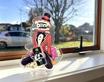 May include: A clear acrylic standee featuring a cartoon character with a top hat, red suit, and bowtie, holding a black rectangular sign with white symbols including a hashtag and percentage sign, set on a circular base.
