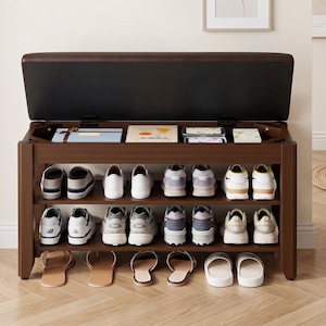 May include: A dark brown wooden shoe storage bench with a hinged, padded seat that opens to reveal a hidden storage compartment. The unit features two open shelves below, currently holding various pairs of sneakers and sandals in organized rows.