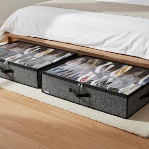 May include: Two gray fabric under-bed shoe storage containers with clear plastic tops, each with a zipper closure and black handles. The containers are positioned under a bed with a white comforter.
