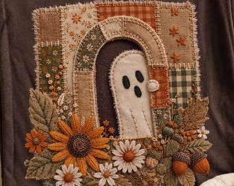May include: A dark brown t-shirt featuring a central rectangular patch design with a ghost peeking through an arched doorway. The design includes patchwork fabric patterns, embroidered sunflowers, daisies, autumn leaves, and acorns in earthy tones.