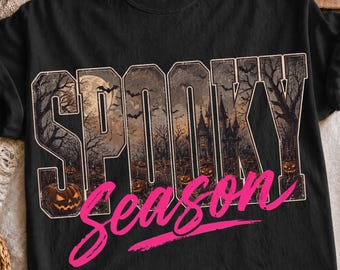 May include: A black t-shirt featuring the word SPOOKY in large block letters filled with a dark forest, a haunted house, bats, and jack-o'-lanterns. The word season is printed below in a bright pink cursive font with a thick underline.