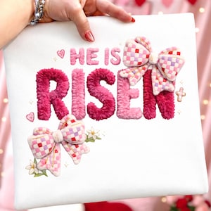 May include: White square fabric featuring the text "HE IS RISEN" in pink, fluffy lettering. The design incorporates two decorative bows with a pink, white, and lavender checkered pattern. Small hearts, stars, and a cross complete the Easter theme.