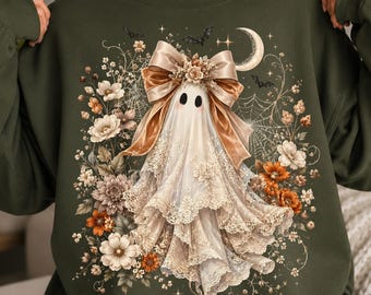 May include: An olive green crewneck sweatshirt featuring a central graphic of a white ghost adorned with a large beige bow and lace trim. The ghost is surrounded by orange and white flowers, a spider web, small bats, and a crescent moon.