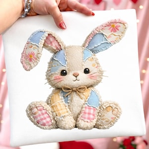 May include: A plush bunny rabbit with patchwork details in pastel colors. The bunny has large, floppy ears, rosy cheeks, and a small bow tie. The patchwork includes floral, gingham, and solid patterns in pink, blue, and yellow. The bunny is sitting on a white surface.