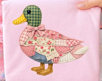 May include: A pink fabric square featuring a patchwork duck design. The duck has a green checkered head, a yellow polka-dot beak, and a pink bow. Its body is made of various patterned fabrics, including floral and gingham prints. The duck has brown feet.