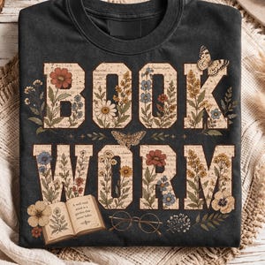 May include: A charcoal gray crewneck t-shirt featuring the text BOOK WORM in large block letters. The letters are filled with a vintage paper pattern, colorful floral illustrations, and butterflies. An open book and round glasses are printed below.