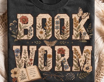 May include: A charcoal gray crewneck t-shirt featuring the text BOOK WORM in large block letters. The letters are filled with a vintage paper pattern, colorful floral illustrations, and butterflies. An open book and round glasses are printed below.