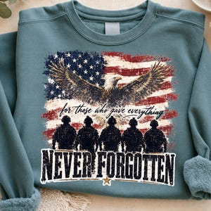 May include: Teal sweatshirt with an American flag design, an eagle, soldiers, and the text "for those who gave everything" and "NEVER FORGOTTEN". The design is in red, white, blue, and gold.