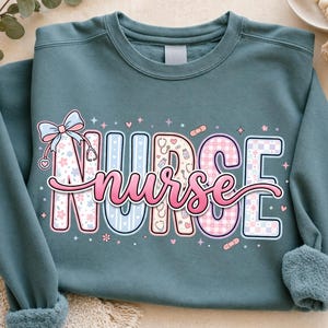 May include: A teal sweatshirt with the word "NURSE" in a colorful, decorative font. The letters are filled with patterns, including flowers, plaid, and medical symbols. A pink cursive "nurse" is written below the word "NURSE". A bow and hearts are also included.