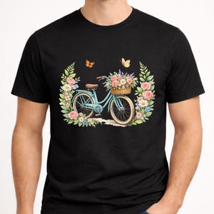 May include: Black t-shirt with a light blue bicycle design, complete with a basket of flowers. The bicycle is set within a floral wreath of pink and white roses, green leaves, and butterflies. A delightful image.
