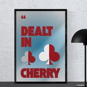 May include: Framed art print featuring the text "DEALT IN CHERRY" in red, and two club symbols. The background has a blue and white gradient. The print is in a black frame.