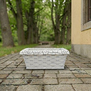 May include: A rectangular white planter with a woven basket texture on the sides and a decorative border of sculpted flowers and leaves along the top rim. The base of the planter features a rope-like trim detail, creating a structured design.