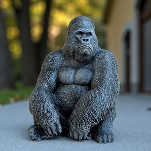 May include: A detailed statue of a gorilla in a seated position. The sculpture is primarily gray with textured details, showcasing the gorilla's muscular build and facial features. The gorilla is sitting with its arms resting on its knees.