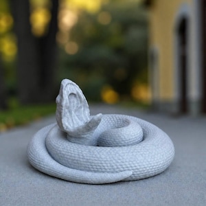 May include: A light gray, coiled snake figurine with a textured, scale-like surface. The snake is depicted in a defensive posture with its mouth wide open, revealing the interior of its throat. The sculpture has a matte finish and a solid form.