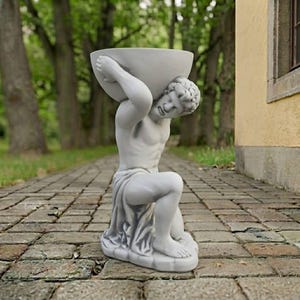 May include: A light gray stone-colored garden statue depicting a kneeling figure with a muscular build, draped in fabric, holding a large, deep, bowl-shaped basin above its head with both hands. The sculpture is crafted in a classical style.