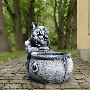 May include: A gray stone-colored garden planter shaped like a gargoyle leaning over a round cauldron. The gargoyle has a weathered, textured finish with dark shading, and the cauldron features a small ring handle detail on its side.