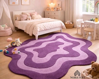 Könnte beinhalten: Ein lila und lavendelfarbener Teppich mit Wellenmuster in einem Kinderzimmer. Der Teppich besteht aus einem weichen Material und liegt auf einem Holzboden. Das Zimmer verfügt außerdem über ein Bett, einen kleinen Tisch und ein Spielzelt.