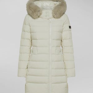May include: Cream-coloured, long puffer coat with a fur-trimmed hood. The coat features a zip-up front, two pockets, and a quilted design. The fur trim is a light brown colour. The coat is a mid-length style.
